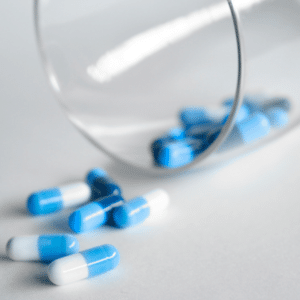 blue and white capsule pills spilling out of clear glass on white table